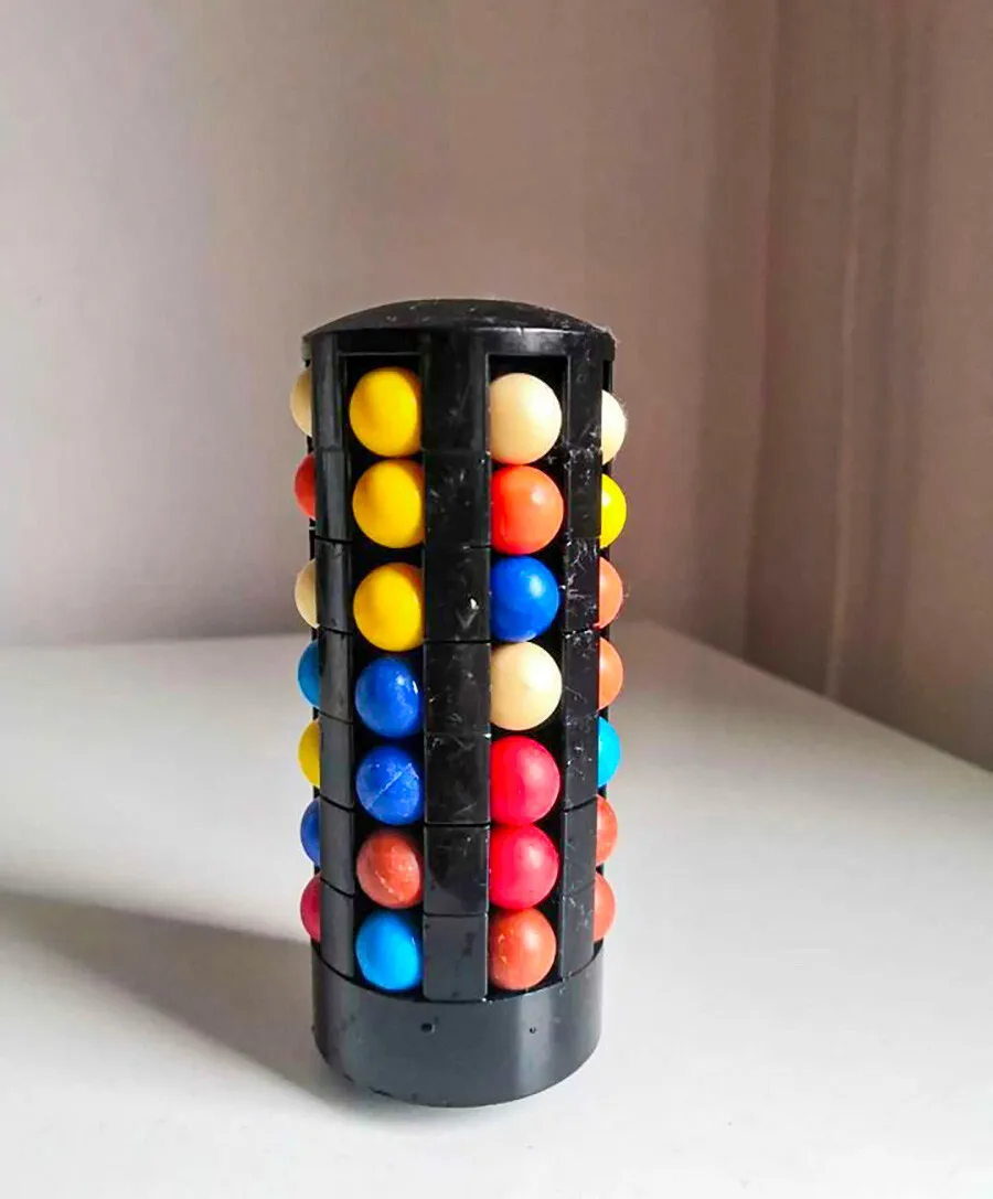 A cylindrical black puzzle toy filled with colorful balls in rows, resting on a plain surface